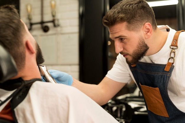 Young man getting his beard styled at the barber