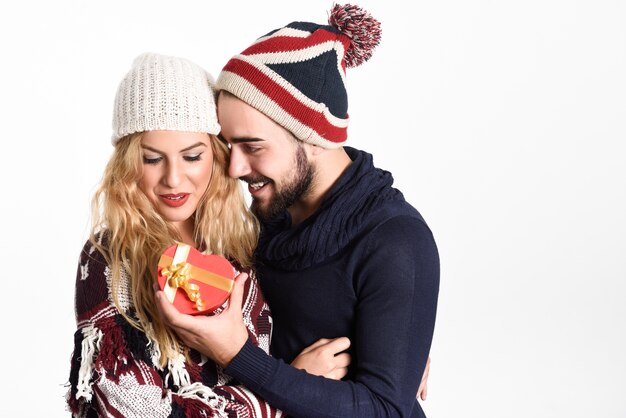 Young man giving a christmas gift to his woman under snow dresses with winter clothes on white background