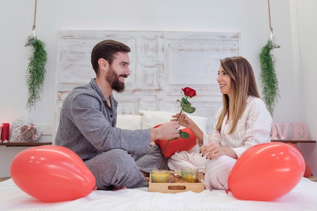 Young man giving red rose to woman on bed