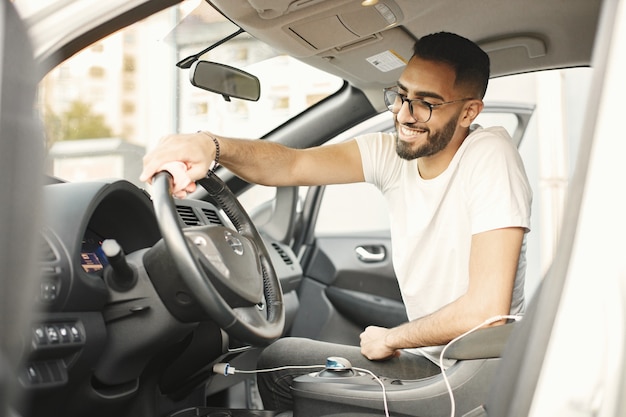 敷物で彼の車の中で磨いている眼鏡の若い男。白いTシャツを着ている男