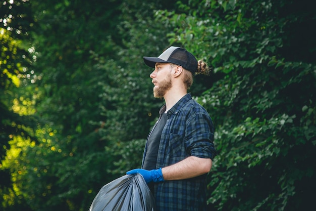 Free photo a young man in gloves and with a garbage bag cleans up in the forest