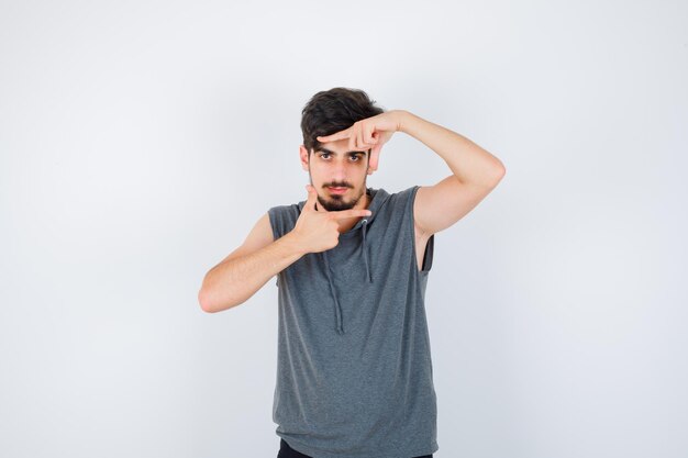 Young man in gray shirt showing frame gesture and looking serious