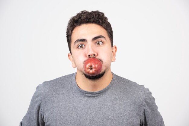 Young man in gray sweatshirt posing with red apple on gray.