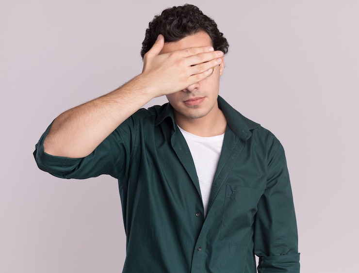 Free Photo young man in green shirt tired and bored closing eyes with hand standing over white wall