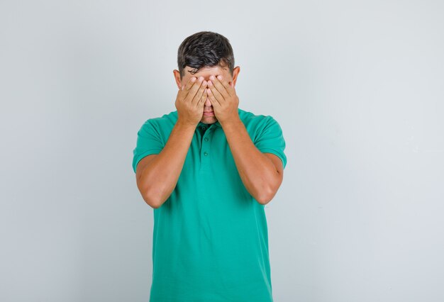 Young man in green t-shirt covering his eyes and looking excited, front view.