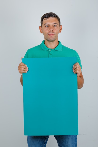 Young man in green t-shirt holding blue poster, front view.