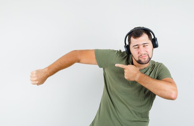 Young man in green t-shirt pointing to side while enjoying music and looking frisky