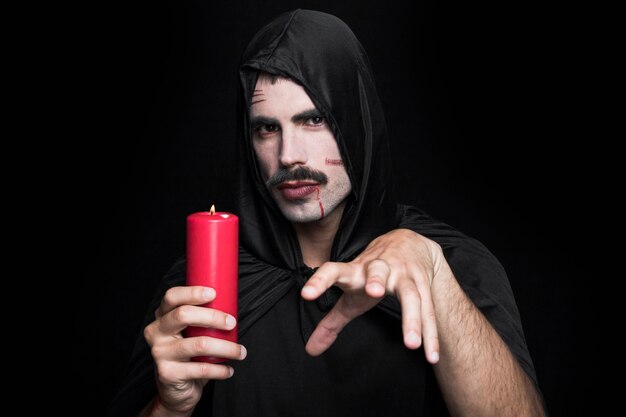 Young man in Halloween costume holding candle with mysterious face