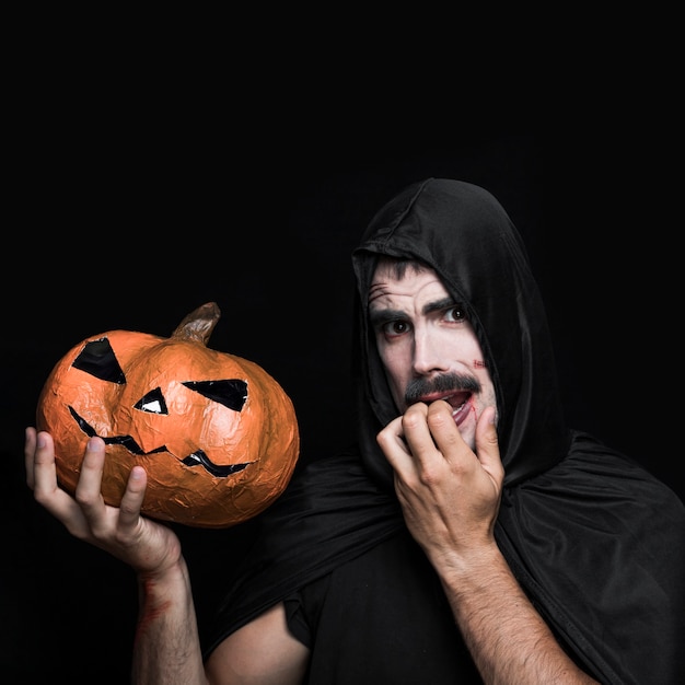 Foto gratuita giovane in costume di halloween tenendo la zucca con la faccia spaventata