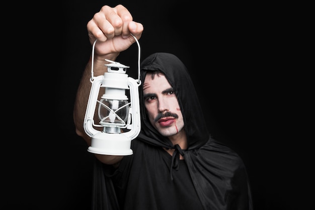 Young man in Halloween costume posing in studio with lantern