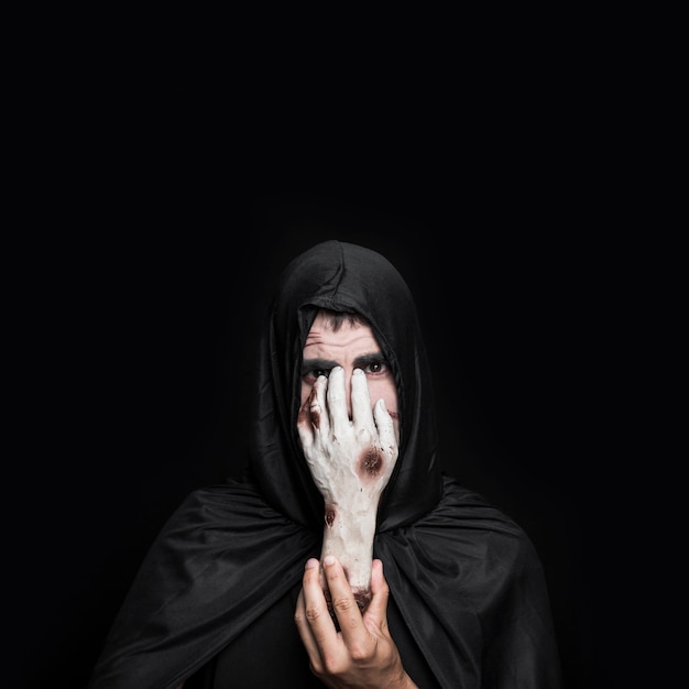 Young man in Halloween costume with hood holding corpse hand