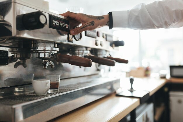 Руки молодого человека работают с кофемашиной в кафе Закройте руки бариста, готовящего кофе за прилавком в ресторане