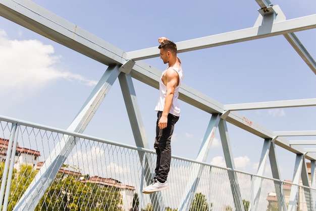 Young man hanging with his one hand on bridge