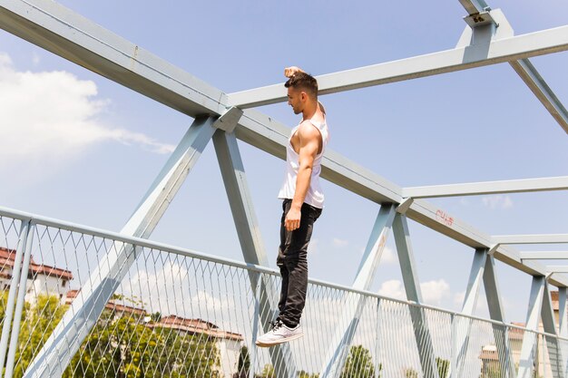 Молодой человек, висящий одной рукой на мосту