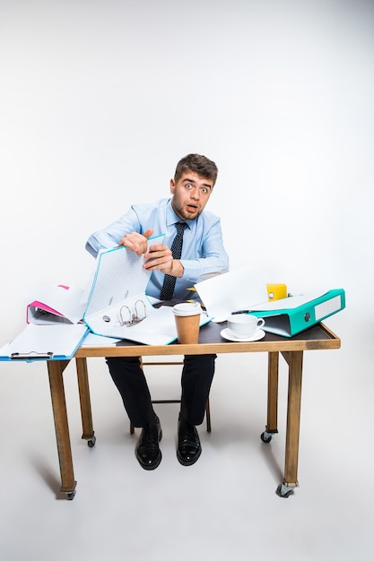 The young man has a complete mess in the workplace, he cannot organize his space and find important documents. Concept of office worker's troubles, business, advertising, everyday problems.