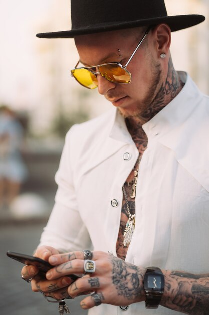 A young man in a hat and sunglasses holds a mobile phone in his hands