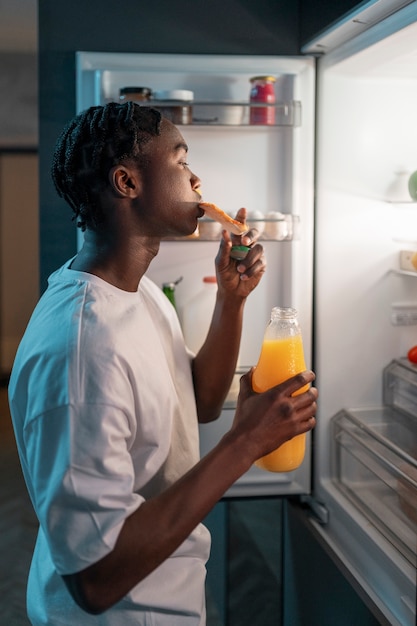 무료 사진 냉장고 옆에 있는 집에서 한밤중에 간식을 먹고 있는 청년