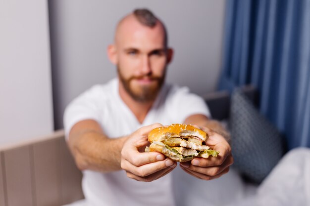 Young man having fast food at home in bedroom on bed