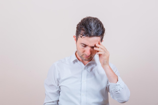 Young man having headache in white shirt and looking fatigued