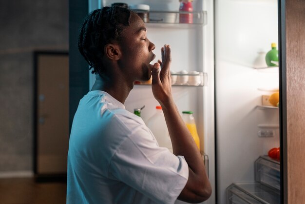 young man having a snack in the middle of the night at home next to fridge