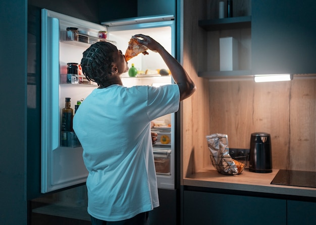 Free photo young man having a snack in the middle of the night at home next to fridge