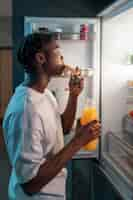 Free photo young man having a snack in the middle of the night at home next to fridge