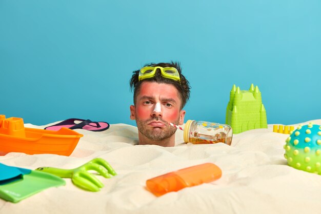 Young man head with sunscreen cream on face surrounded by beach accessories