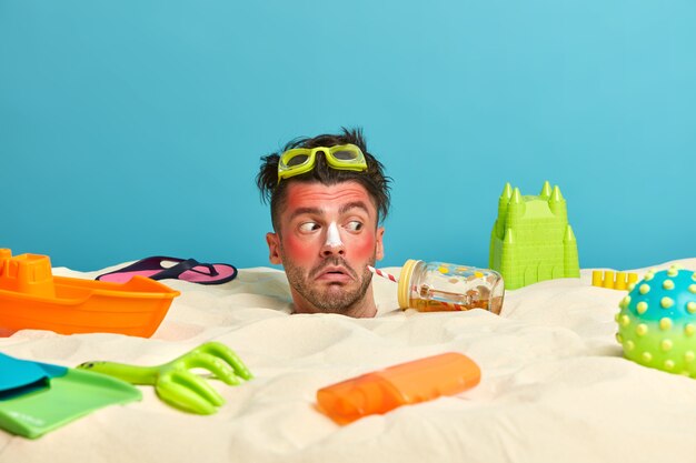 Young man head with sunscreen cream on face surrounded by beach accessories