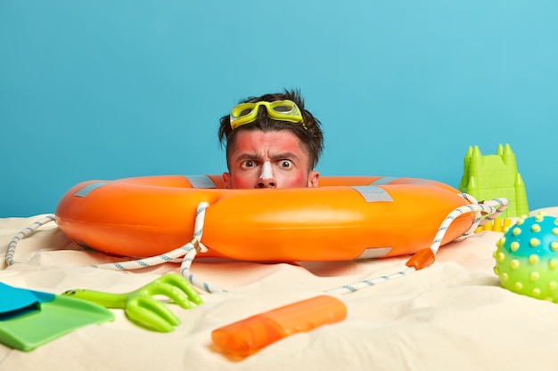 Free photo young man head with sunscreen cream on face surrounded by beach accessories