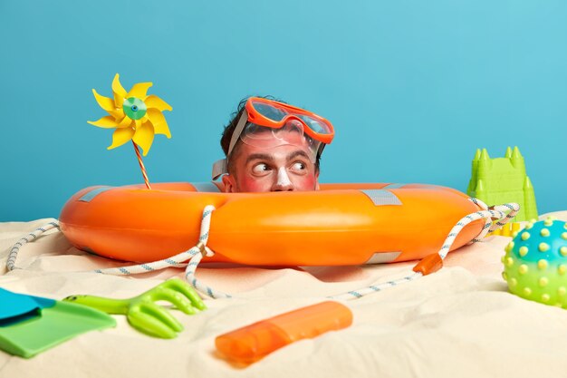 Young man head with sunscreen cream on face surrounded by beach accessories