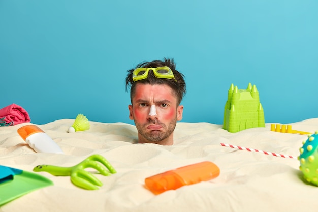 Young man head with sunscreen cream on face surrounded by beach accessories