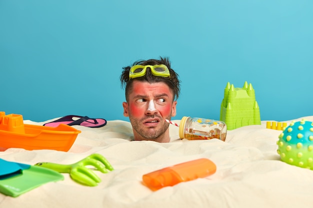 Young man head with sunscreen cream on face surrounded by beach accessories