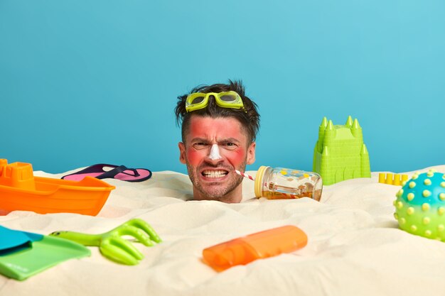 Young man head with sunscreen cream on face surrounded by beach accessories