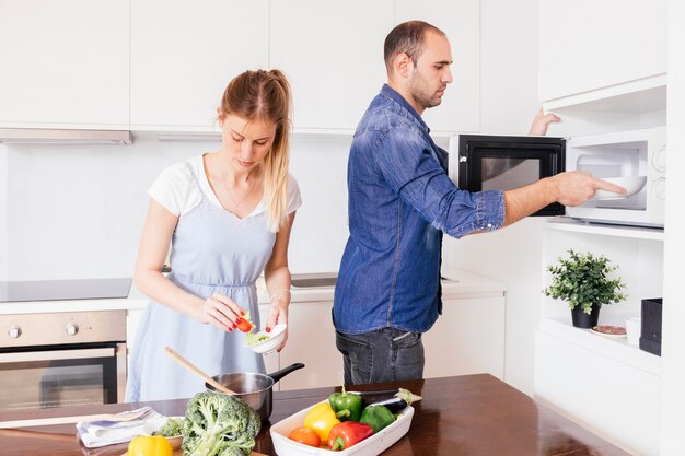 Молодой человек помогает жене готовить еду на кухне