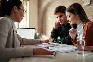 Free photo young man and his wife examining housing plans with real estate agent on a meeting in the office