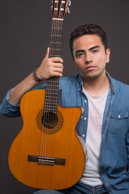 Young man holding a beautiful guitar on black background. High quality photo