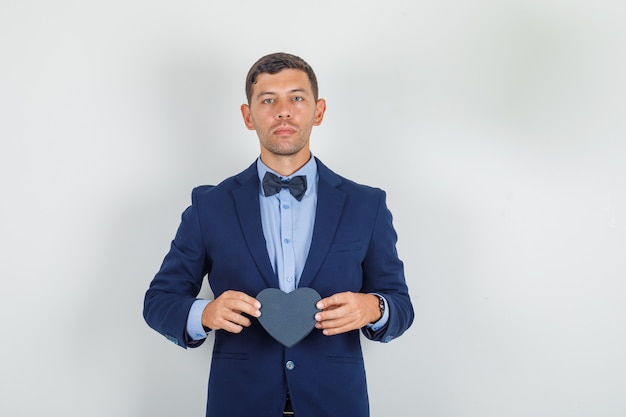 Young man holding black gift box in suit and looking serious