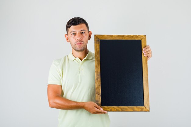 Young man holding blackboard and looking at camera in t-shirt