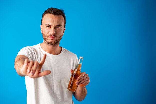 Young man holding a bottle of beer and shows a stop signal