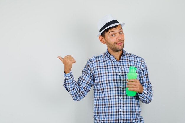 Young man holding bottle for water, pointing away in checked shirt