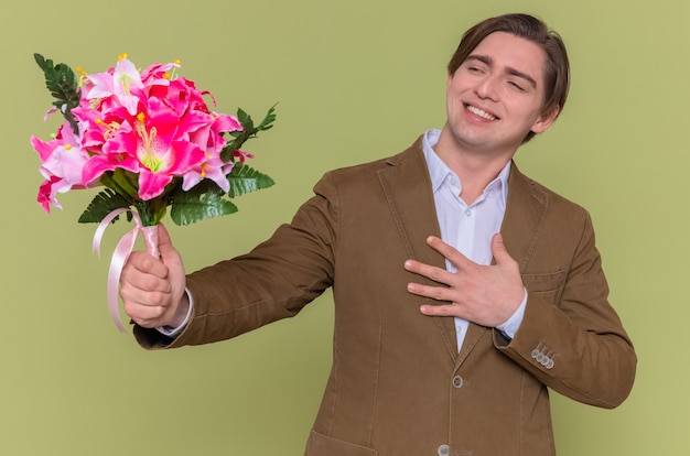 Молодой человек держит букет цветов, глядя в сторону, улыбаясь, чувствуя благодарность