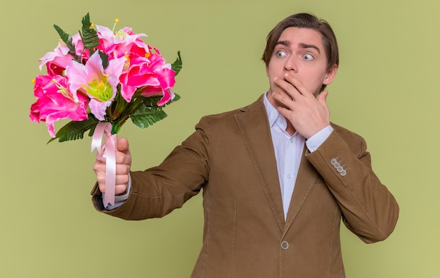 young man holding bouquet of flowers looking at it surprised covering mouth with hand