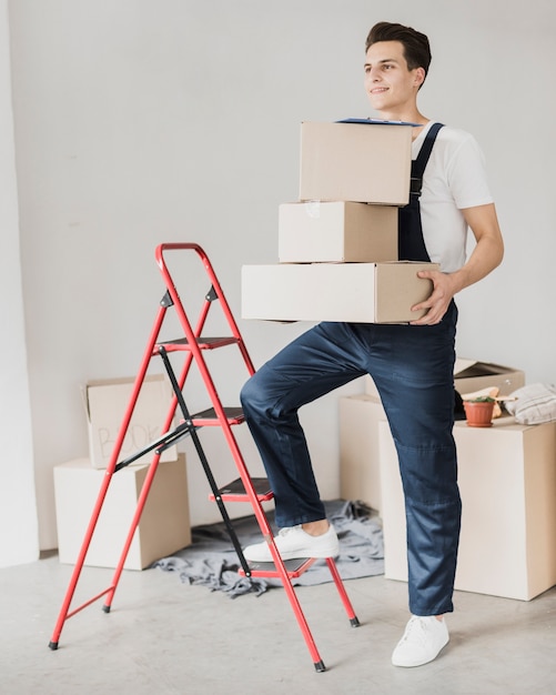Young man holding boxes with foot on ladder