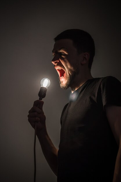 Молодой человек держит в руке горящую лампочку на черном фоне концепции идеи