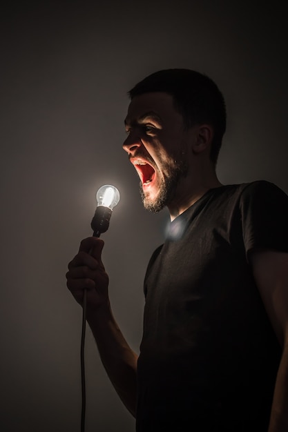 a young man holding a burning light bulb in hand on black background concept ideas