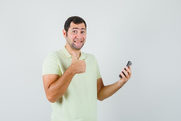 Молодой человек, держащий калькулятор, показывает палец вверх в футболке и выглядит весело