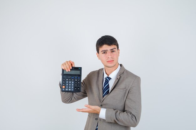 Young man holding calculator, stretching hand as presenting it in formal suit