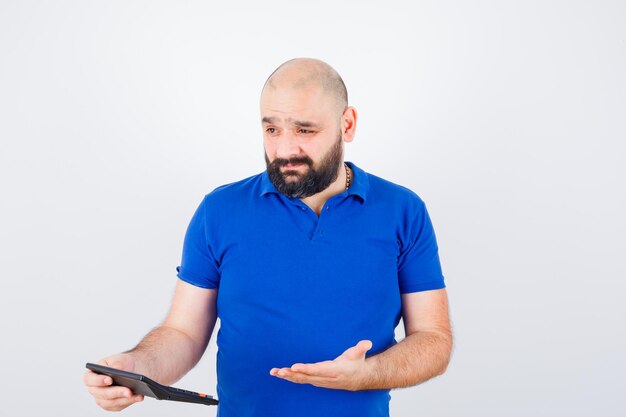 Young man holding calculator while discussing in blue shirt and looking focused , front view.