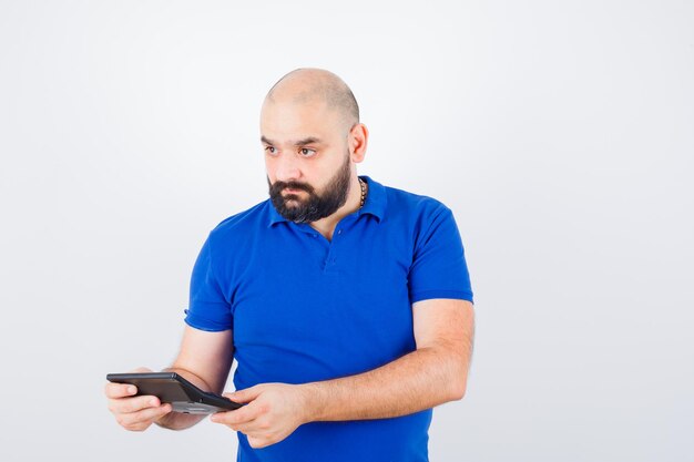 Young man holding calculator while looking away in blue shirt and looking focused. front view.