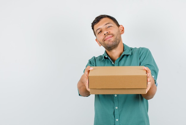 Young man holding cardboard box and smiling in shirt